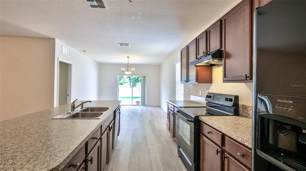 A kitchen with dark wood cabinets, laminate countertops, and stainless steel appliances overlooks a dining area — 346 ADMIRALTY COURT, EDGEWATER, FL