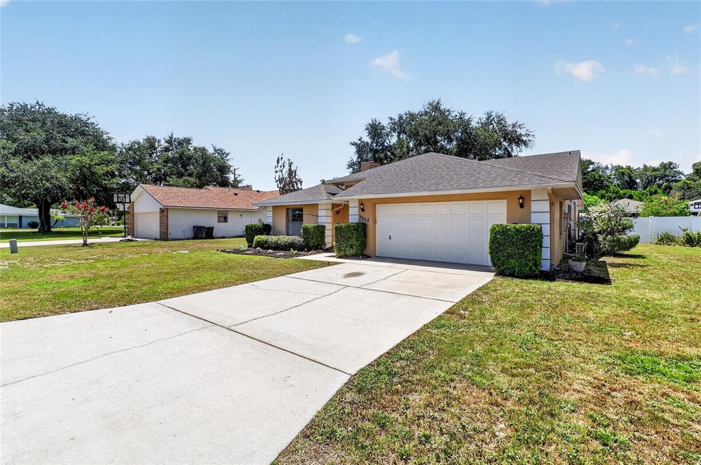 A single-story house with a white garage door, tan stucco exterior, and a concrete driveway — 1202 VALENCIA LANE, AUBURNDALE, FL