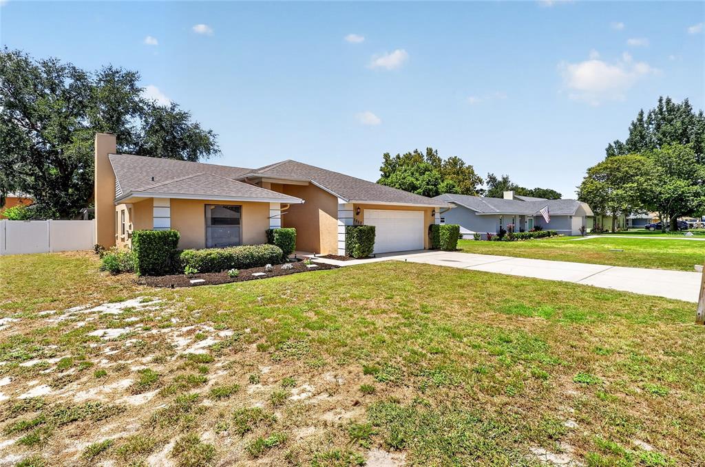 A tan single-story house with a two-car garage and a large front lawn — 1202 VALENCIA LANE, AUBURNDALE, FL