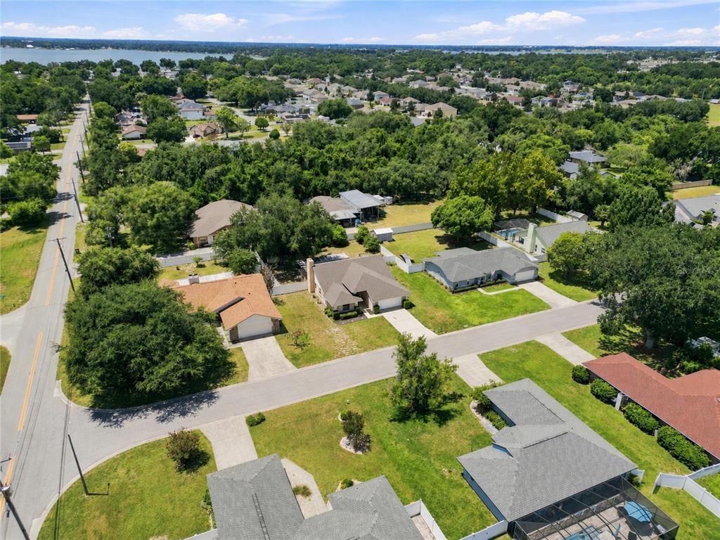 An aerial view shows several suburban houses with driveways, lawns, and trees near a lake — 1202 VALENCIA LANE, AUBURNDALE, FL
