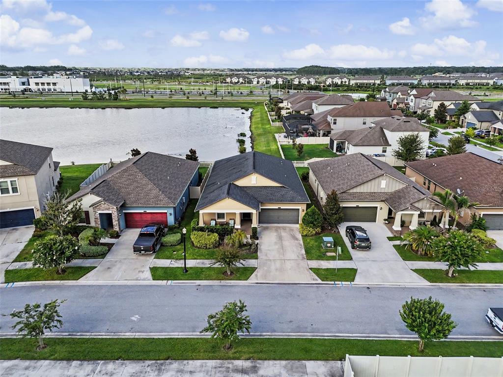 An aerial view shows three suburban houses with driveways facing a street and a lake — 9189 SHADYSIDE LANE, LAND O LAKES, FL
