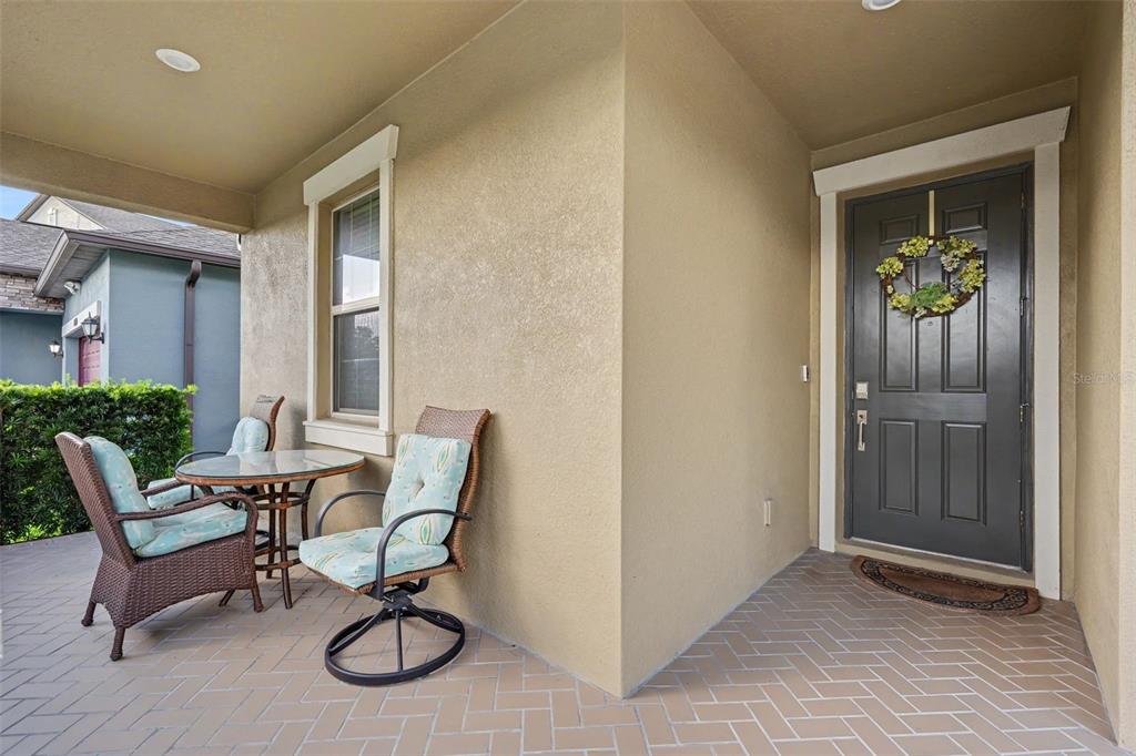 A covered front porch features a small glass table, two wicker chairs, and a dark door — 9189 SHADYSIDE LANE, LAND O LAKES, FL