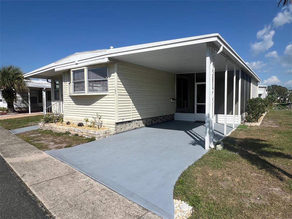 A single-story manufactured home features light siding, a gray painted carport, and a screened porch — 103 PINDO PALM STREET W, LARGO, FL