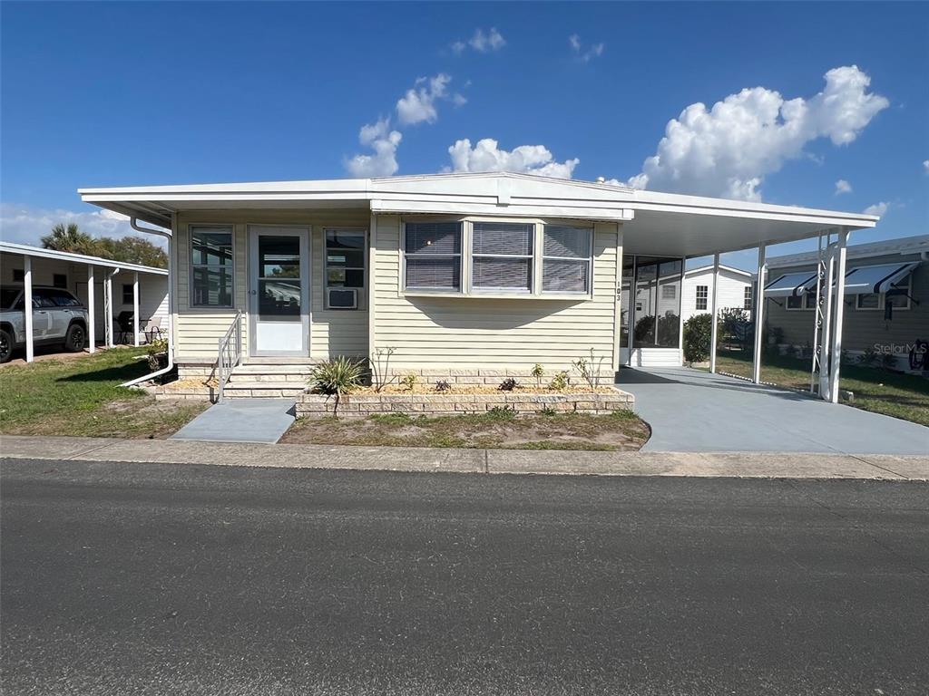A light-colored mobile home features a front entrance, a bay window, and a covered carport — 103 PINDO PALM STREET W, LARGO, FL