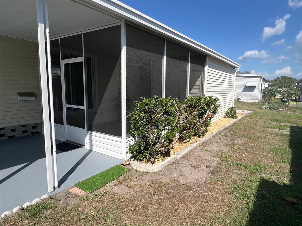 A screened-in porch with a gray floor sits beside a house with light-colored siding — 103 PINDO PALM STREET W, LARGO, FL