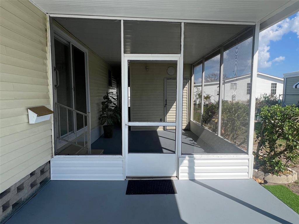 A screened-in porch with a white door, gray flooring, and vinyl siding exterior — 103 PINDO PALM STREET W, LARGO, FL