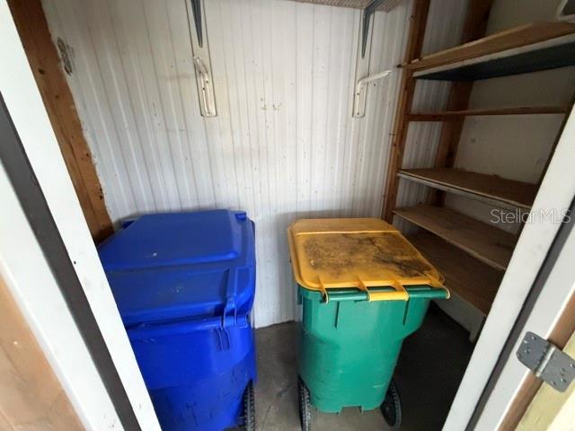 A small storage closet contains two rolling trash bins and wooden shelving units — 1023 SOUTHLAND DRIVE, TAVARES, FL