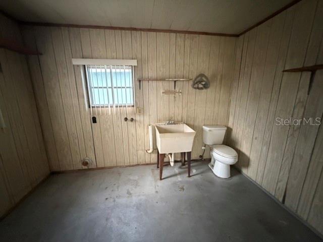 A utility room with wood-paneled walls, a concrete floor, a utility sink, and a toilet — 1023 SOUTHLAND DRIVE, TAVARES, FL