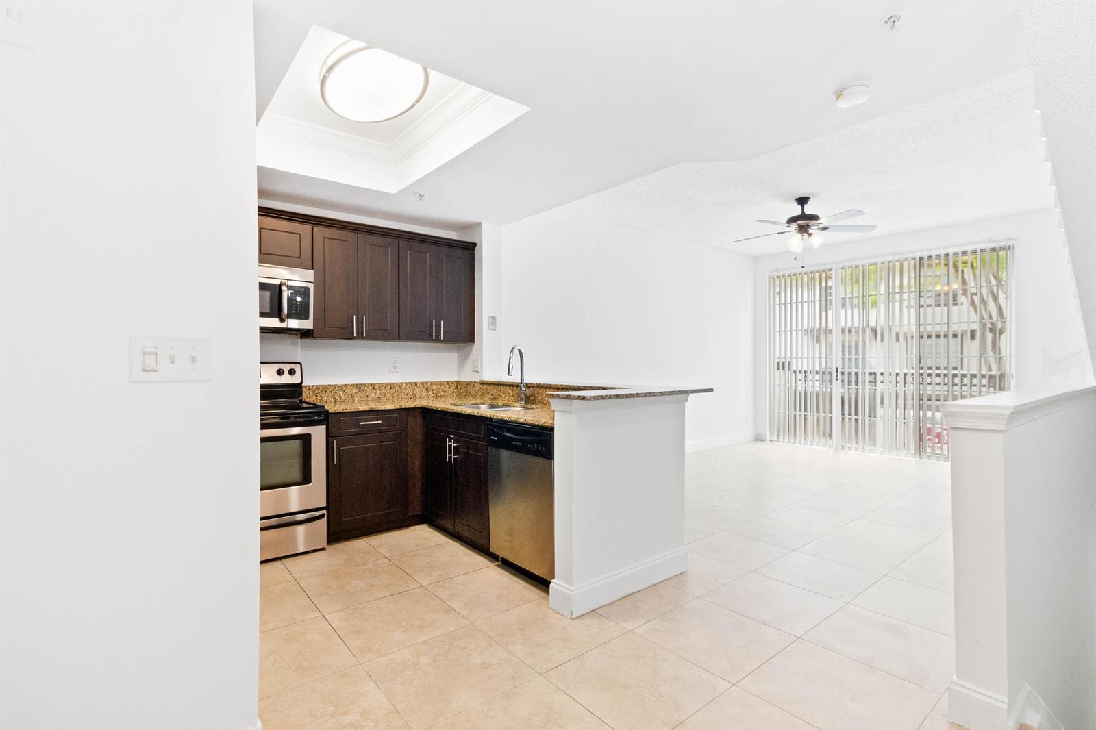 A kitchen with dark cabinets and granite countertops opens into a tiled living area — 20889 Saint Andrews Boulevard, Boca Raton FL 33433, BOCA RATON, FL