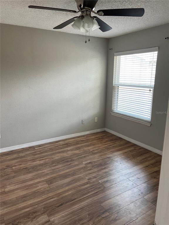 An empty bedroom features wood-look flooring, light gray walls, a ceiling fan, and a window — 3740 IDLEBROOK CIRCLE UNIT 202, CASSELBERRY, FL