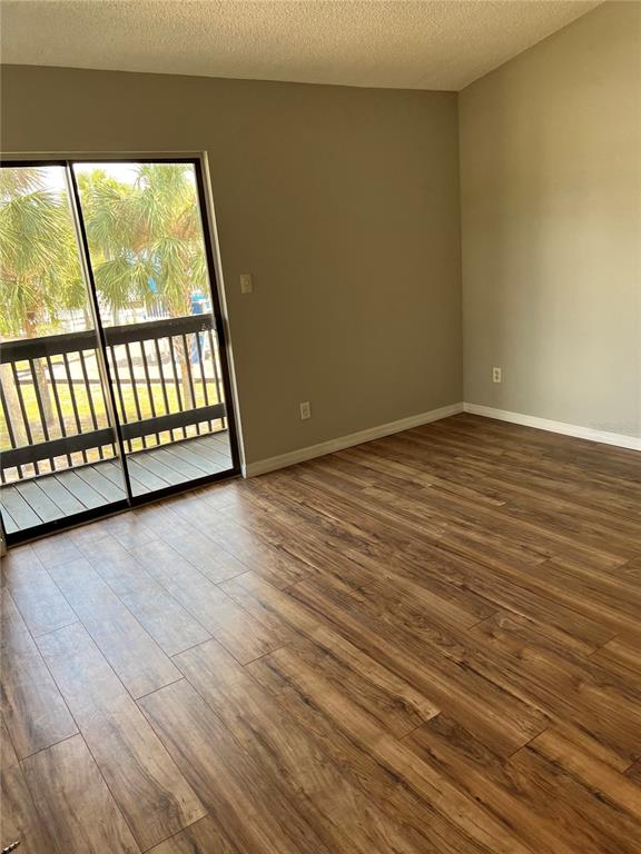 An empty room features wood-look flooring, beige walls, and a sliding glass door to a balcony — 3740 IDLEBROOK CIRCLE UNIT 202, CASSELBERRY, FL