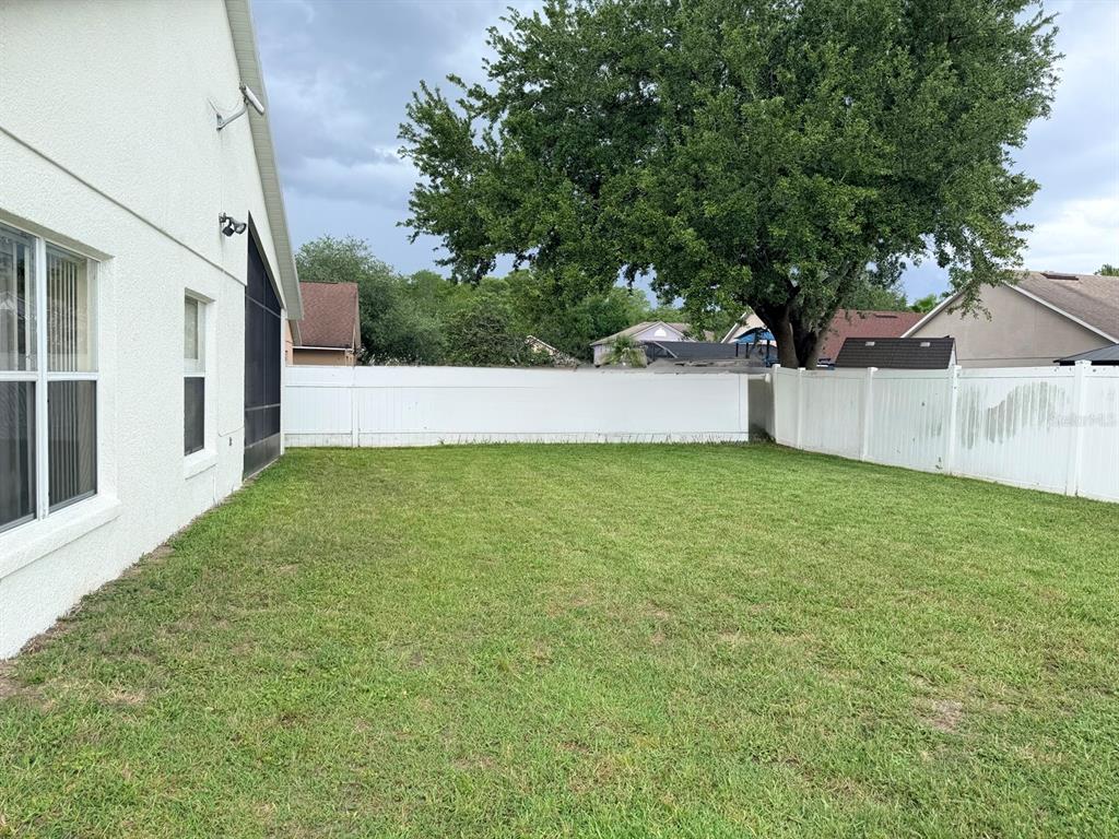A grassy backyard features a white vinyl fence and a large tree — 3513 MCALLISTER WAY, ORLANDO, FL