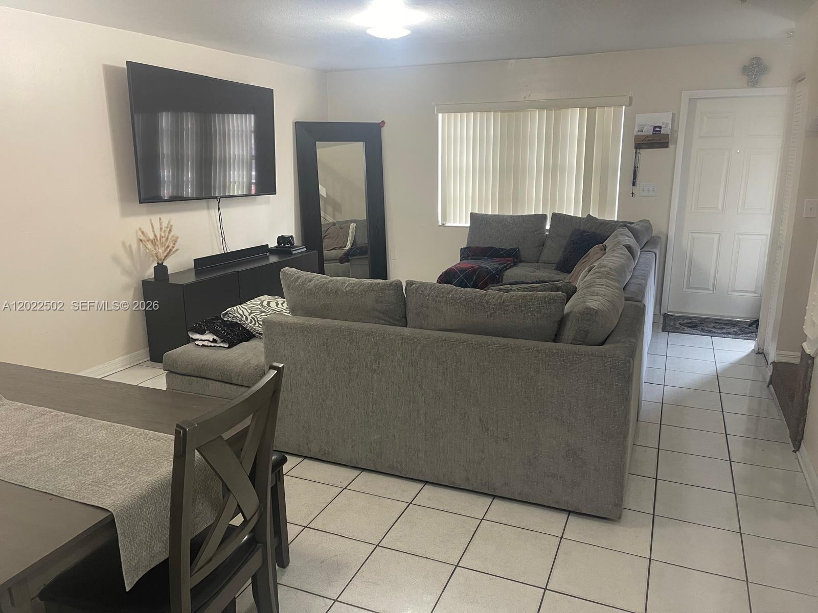 A living room features a large gray sectional sofa, a wall-mounted television, and tiled flooring — 9880 Hammocks Blvd # 43, Miami FL 33196, MIAMI, FL