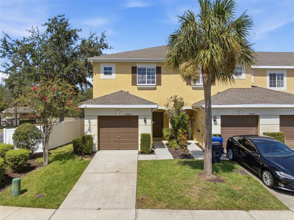 A two-story yellow townhouse with a brown garage door and a palm tree in front — 20402 NEEDLETREE DRIVE, TAMPA, FL