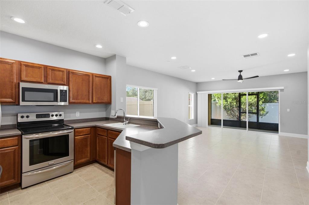 A kitchen with wood cabinets and stainless steel appliances opens to a tiled living area — 20402 NEEDLETREE DRIVE, TAMPA, FL