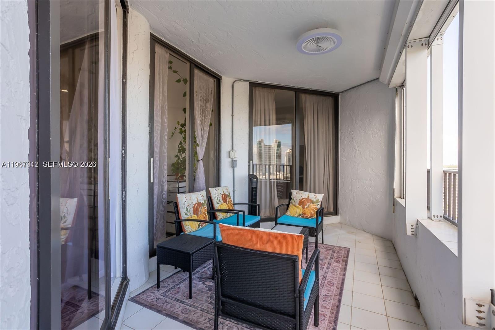 A balcony features tiled flooring, outdoor seating with patterned cushions, and sliding glass doors — 300 Three Islands Blvd, Hallandale Beach FL 33009, HALLANDALE BEACH, FL