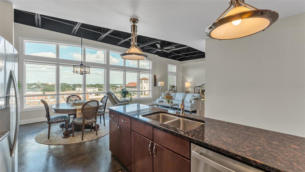 A kitchen island with granite countertops overlooks a dining area and living room with windows — 125 N KENTUCKY AVENUE UNIT 505, LAKELAND, FL