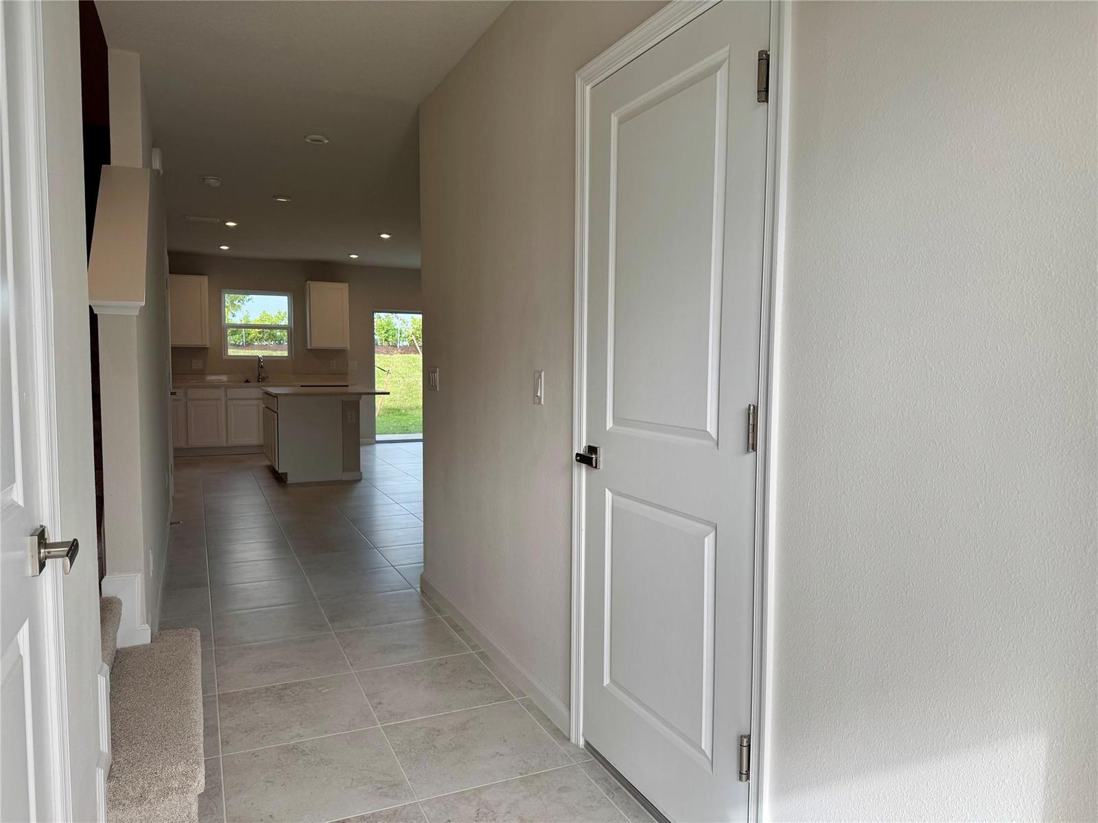 A hallway with tile flooring leads to a kitchen featuring white cabinets and an island — PORT ST. LUCIE, FL