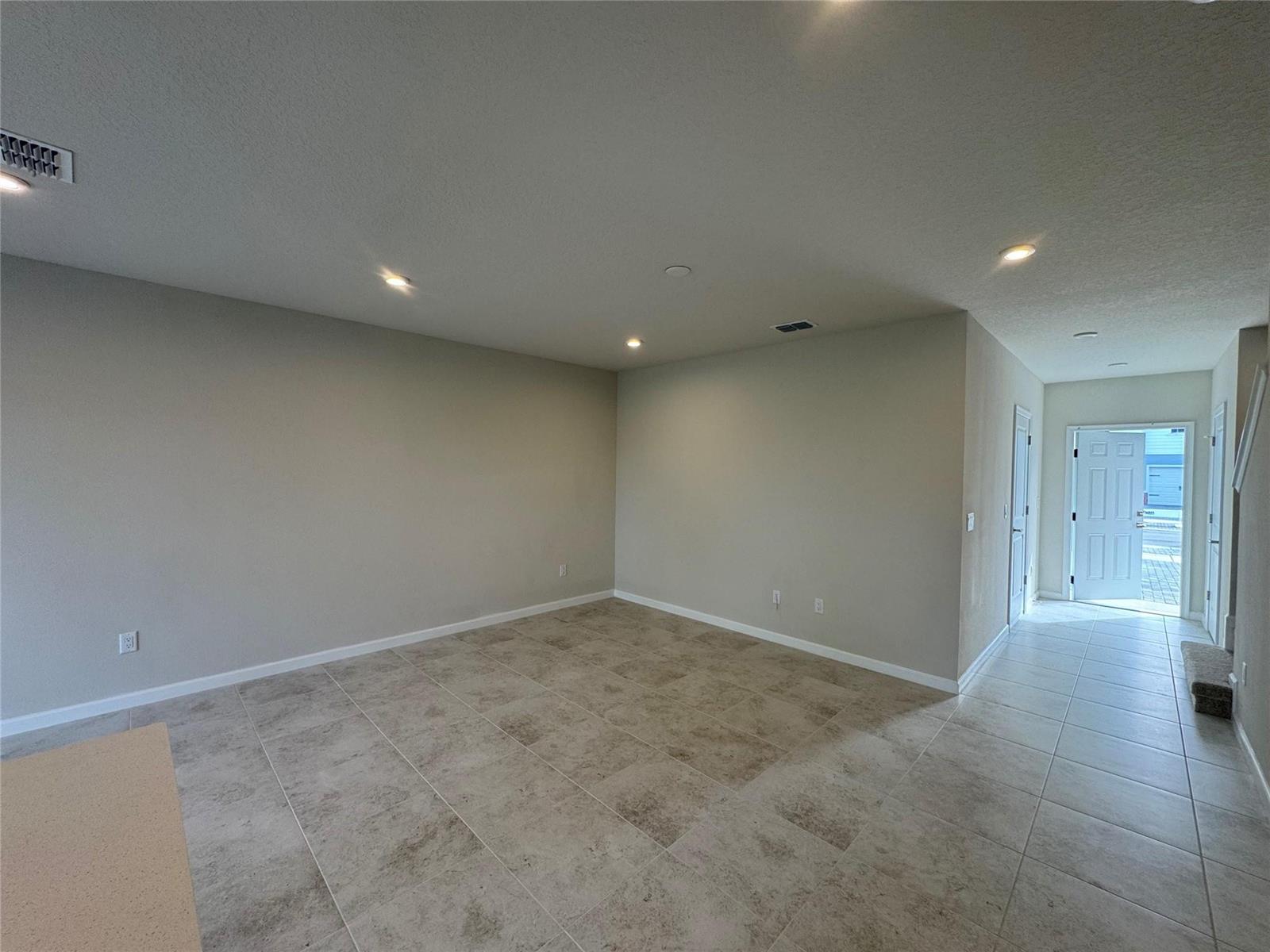 An empty room with beige walls, tile flooring, recessed lighting, and an open front door — PORT ST. LUCIE, FL