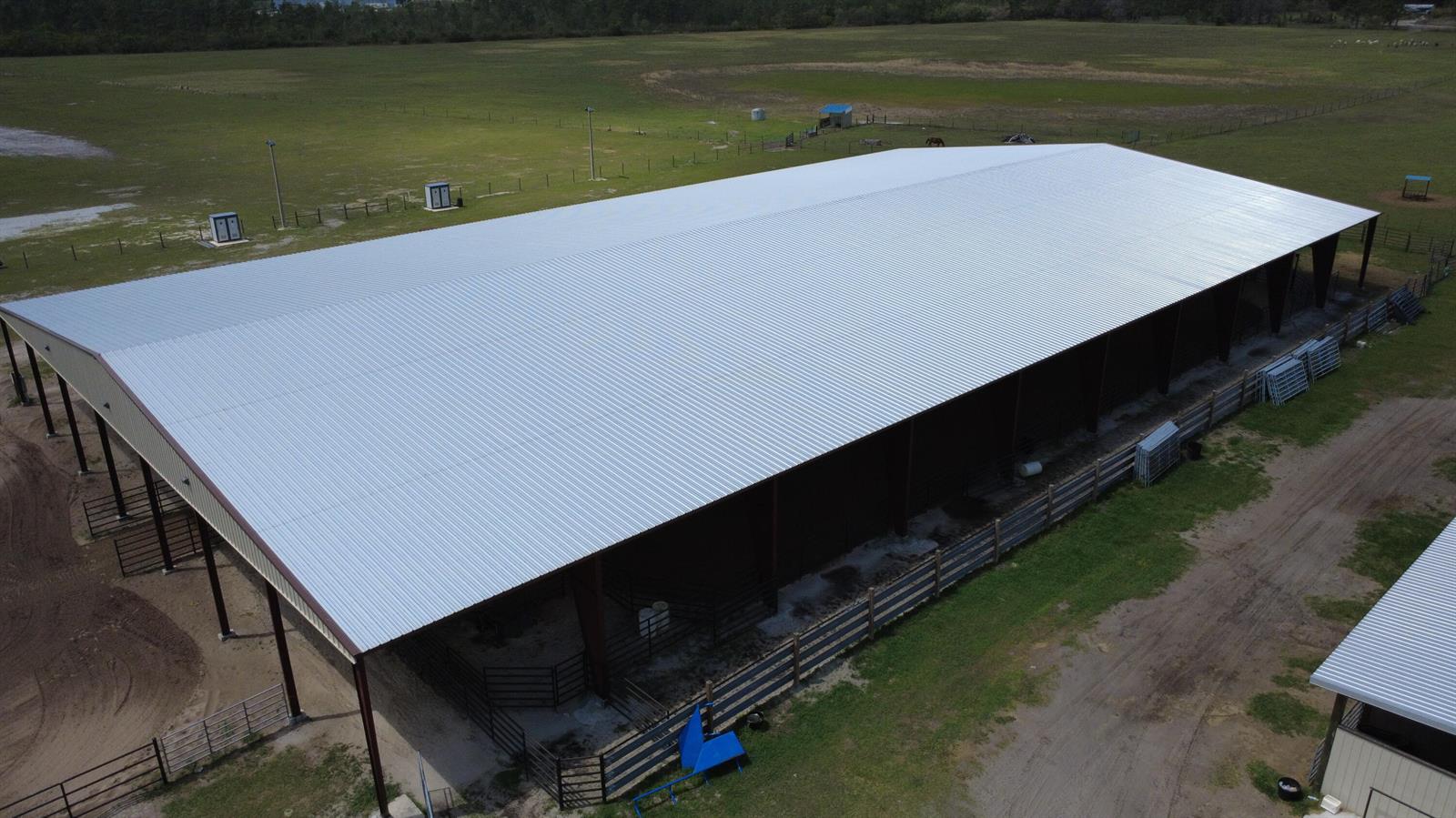 An aerial view shows a large, open-sided metal barn with a corrugated roof on a farm — 33700 Hwy 441, Okeechobee FL 34972, OKEECHOBEE, FL