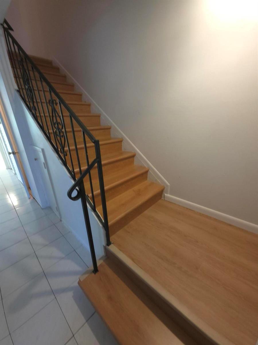 A staircase with light wood steps and a black metal railing leads to an upper level — HALLANDALE BEACH, FL