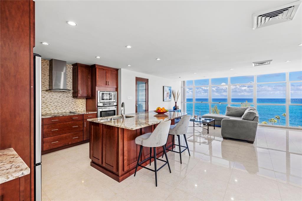 A kitchen with wood cabinets and a granite island overlooks the ocean through floor-to-ceiling windows — 860 ASHFORD AVE UNIT 9, SAN JUAN, PR
