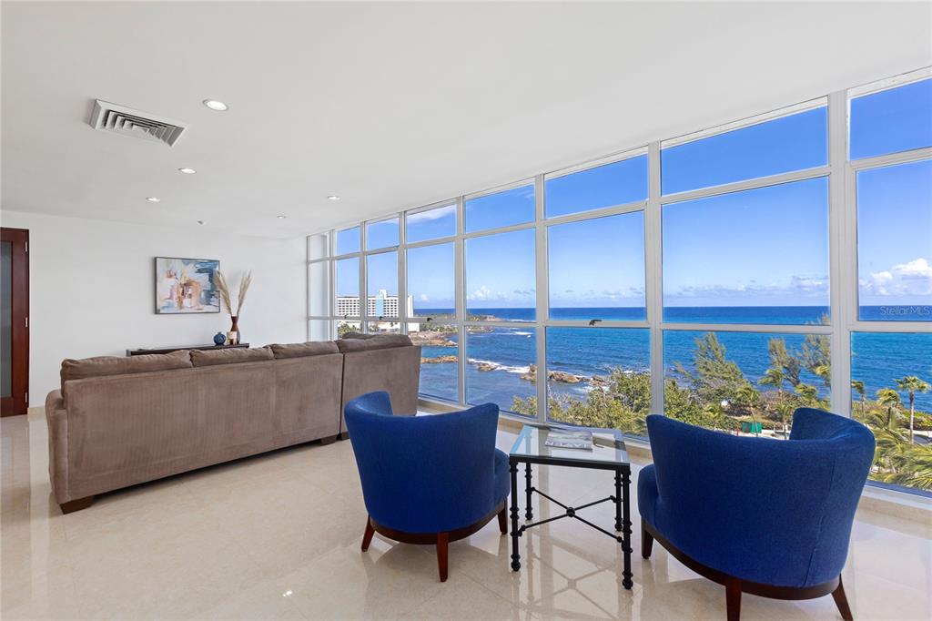 A living room features a large sectional sofa, two blue armchairs, and floor-to-ceiling ocean views — 860 ASHFORD AVE UNIT 9, SAN JUAN, PR
