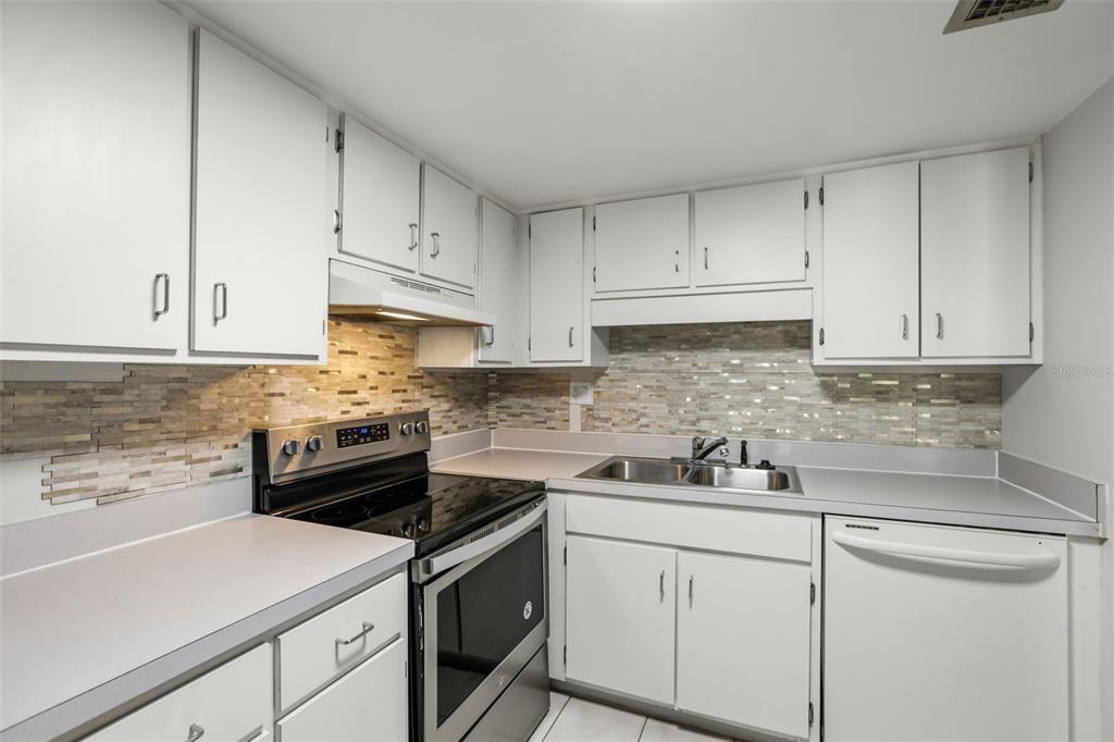 A kitchen features white cabinets, stainless steel appliances, and a multi-colored stone tile backsplash — 200 MAITLAND AVENUE UNIT 20, ALTAMONTE SPRINGS, FL