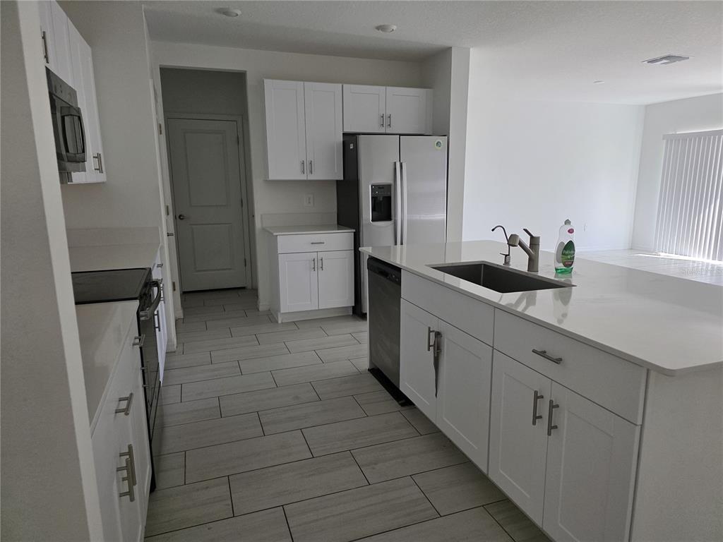 A modern kitchen features white cabinetry, a large central island, and light-colored tile flooring — 12588 TIMBER MOSS LANE, RIVERVIEW, FL