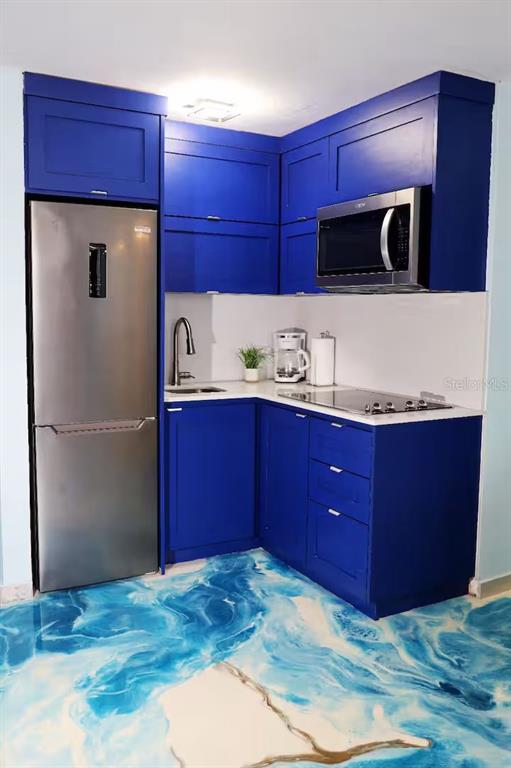 A small kitchen features vibrant blue cabinets, stainless steel appliances, and a swirling blue-patterned floor — 1126 ASHFORD UNIT 27, SAN JUAN, PR