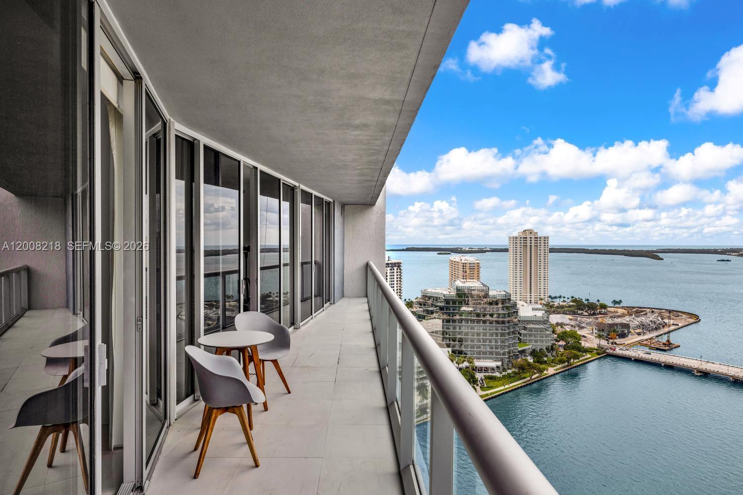 A high-rise balcony features a small table, two chairs, and a panoramic water view — 495 Brickell Ave # 2603, Miami FL 33131, MIAMI, FL