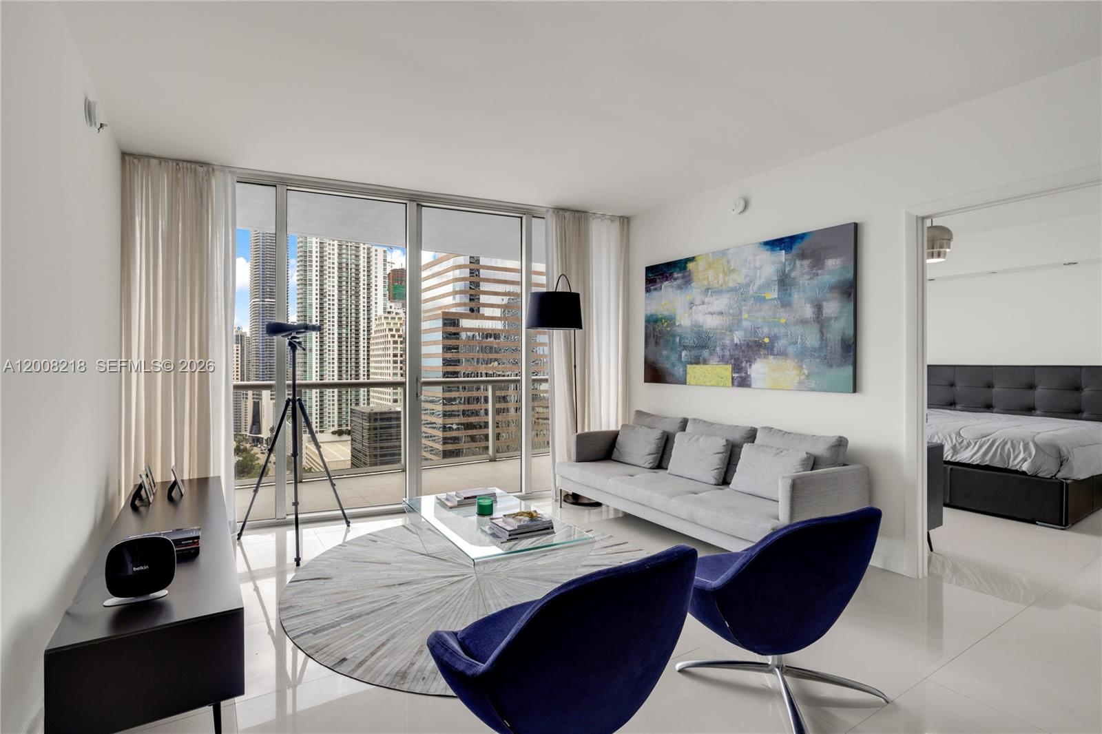 A modern living room features a grey sofa, blue chairs, and floor-to-ceiling windows with city views — 495 Brickell Ave # 2603, Miami FL 33131, MIAMI, FL