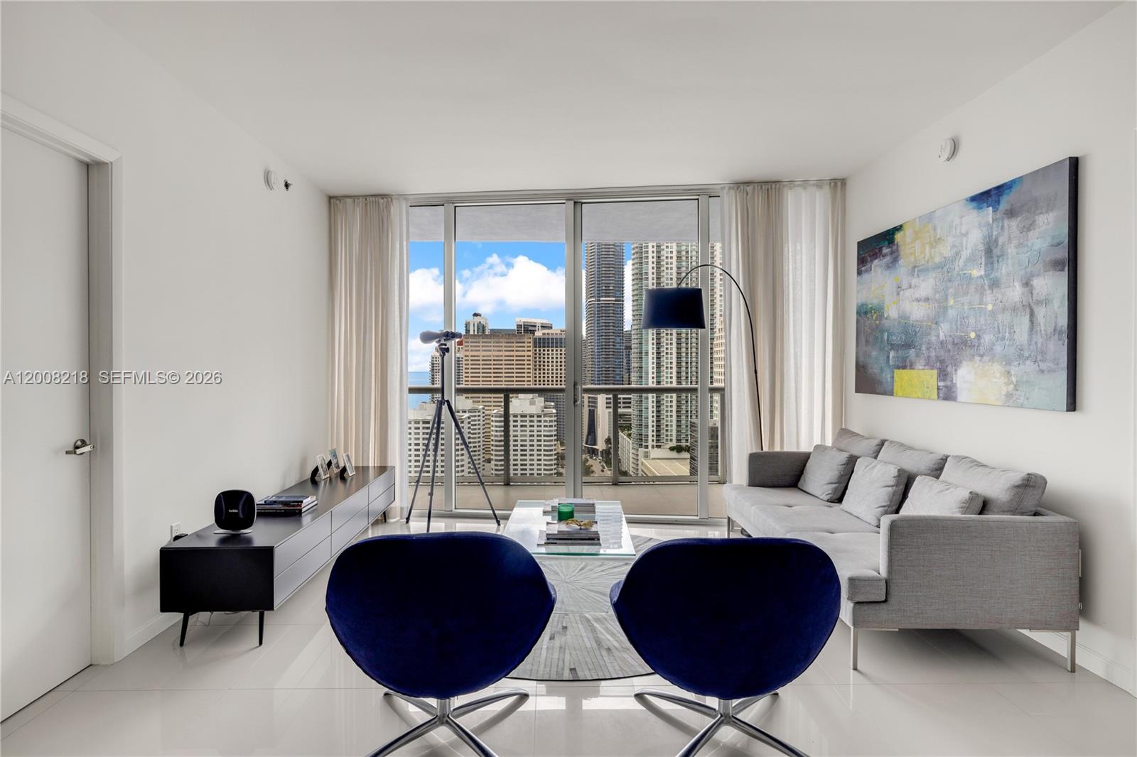 A modern living room features blue chairs, a grey sofa, and a city skyline view — 495 Brickell Ave # 2603, Miami FL 33131, MIAMI, FL