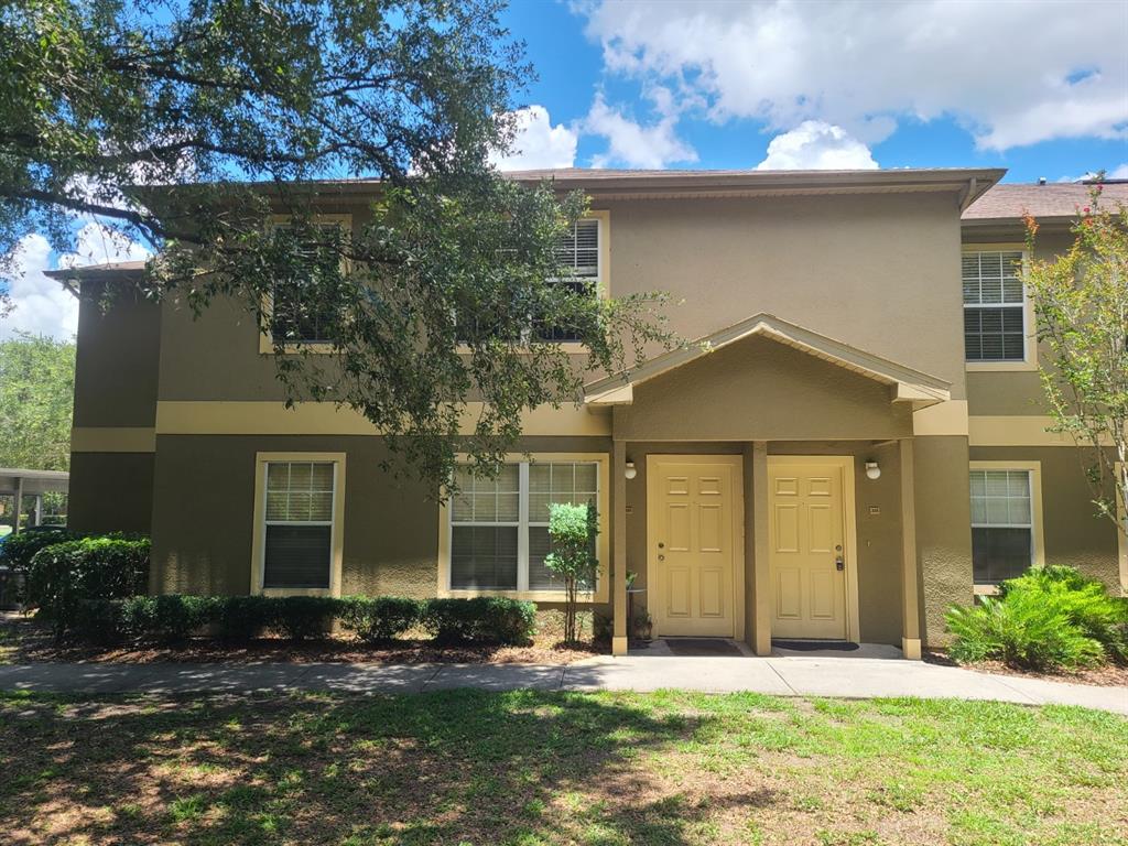 A two-story apartment building with tan stucco walls, two front doors, and a sidewalk — 36122 LAKE CHASE BOULEVARD UNIT 203, ZEPHYRHILLS, FL