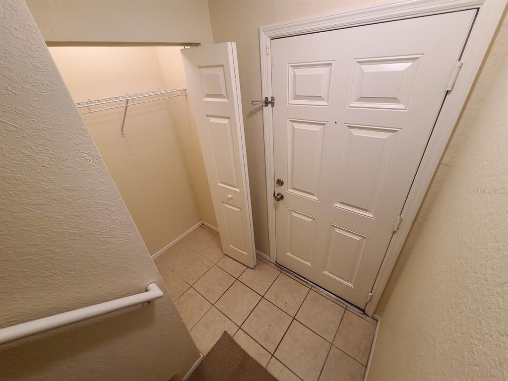 An entryway features a tiled floor, a white front door, and an open coat closet — 36122 LAKE CHASE BOULEVARD UNIT 203, ZEPHYRHILLS, FL