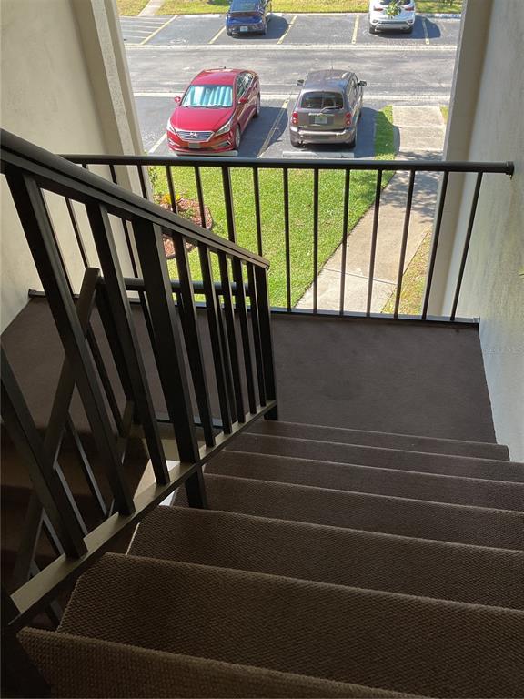 A view looking down a carpeted outdoor staircase toward a parking lot with several cars — 2655 PINE RIDGE WAY N UNIT D3, PALM HARBOR, FL