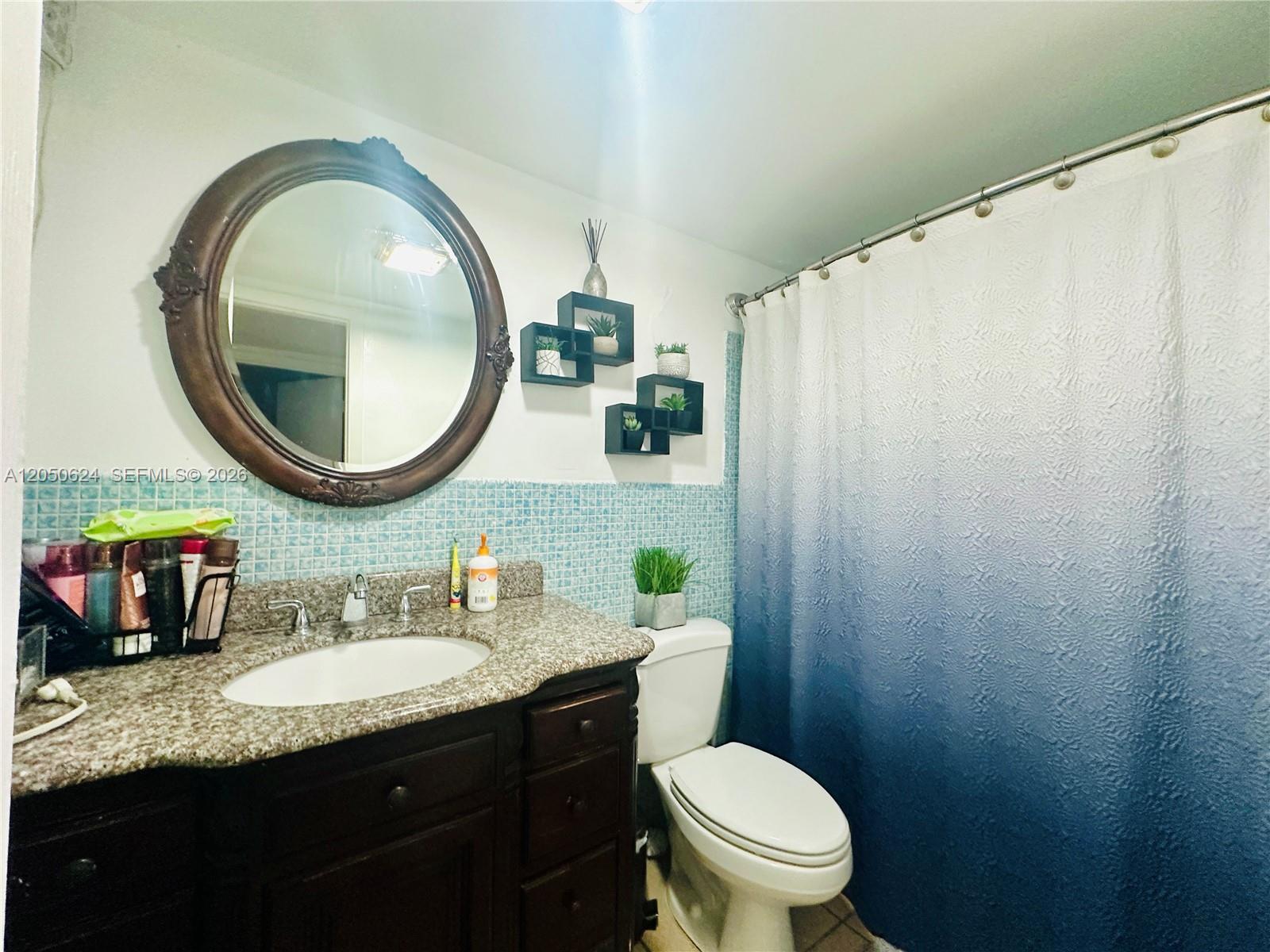 A bathroom features a dark wood vanity, granite countertop, blue mosaic tile, and ombre shower curtain — 6837 W 19th Ct # 6837, Hialeah FL 33014, HIALEAH, FL