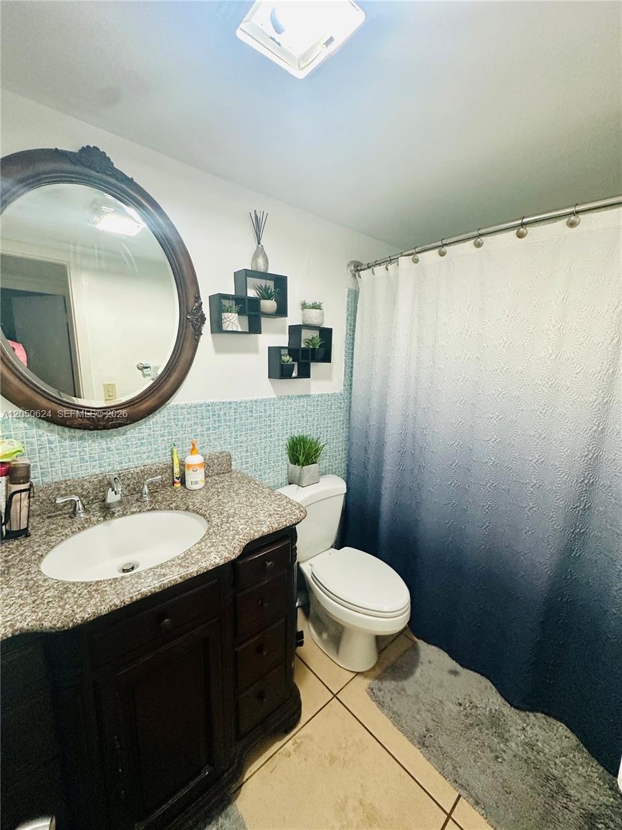 A bathroom features a granite vanity, a round mirror, a toilet, and a blue ombre shower curtain — 6837 W 19th Ct # 6837, Hialeah FL 33014, HIALEAH, FL