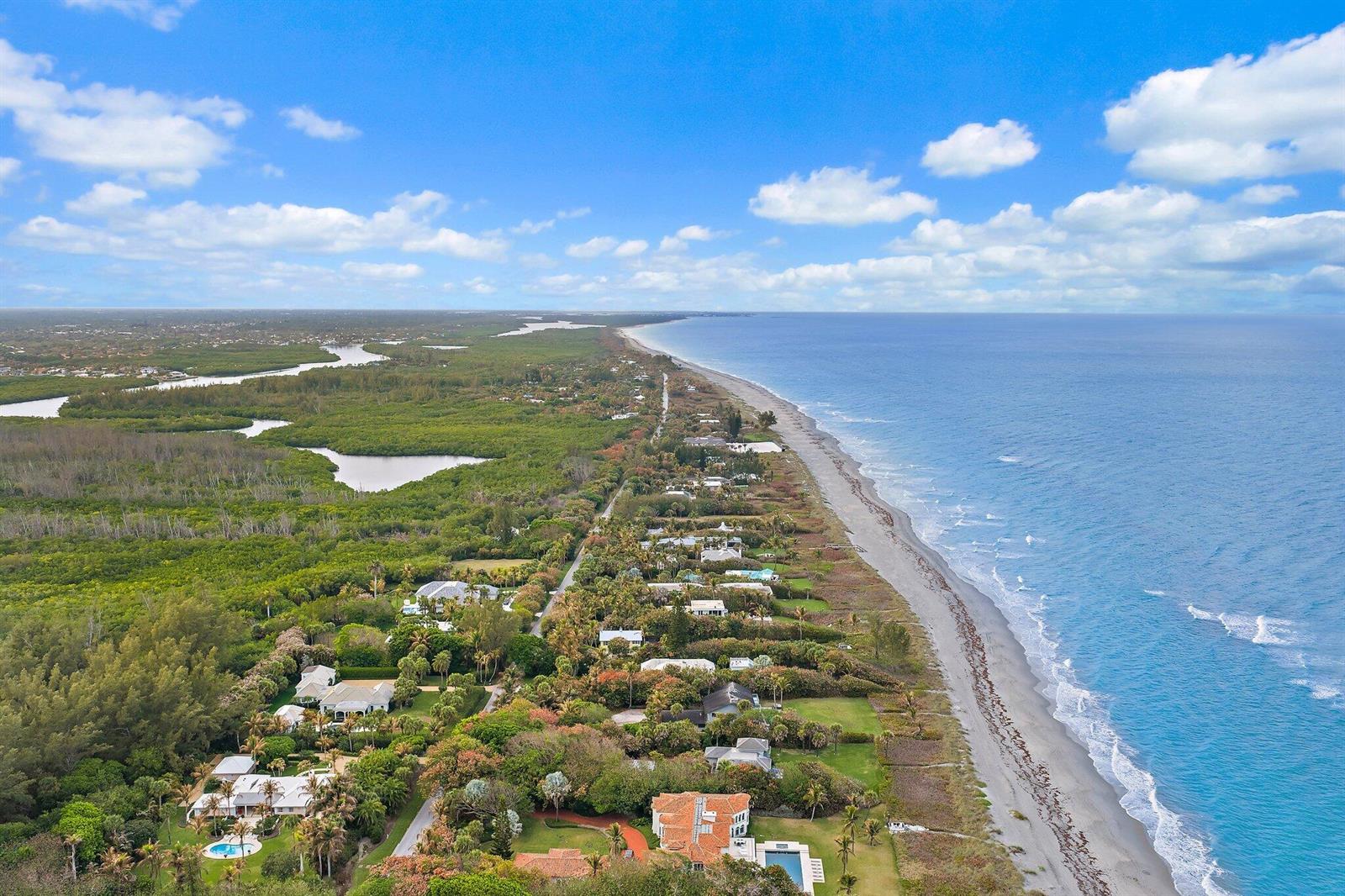 An aerial view shows coastal homes nestled between a lush forest and the ocean beach — 31 N Beach Road, Jupiter Island FL 33455, JUPITER ISLAND, FL