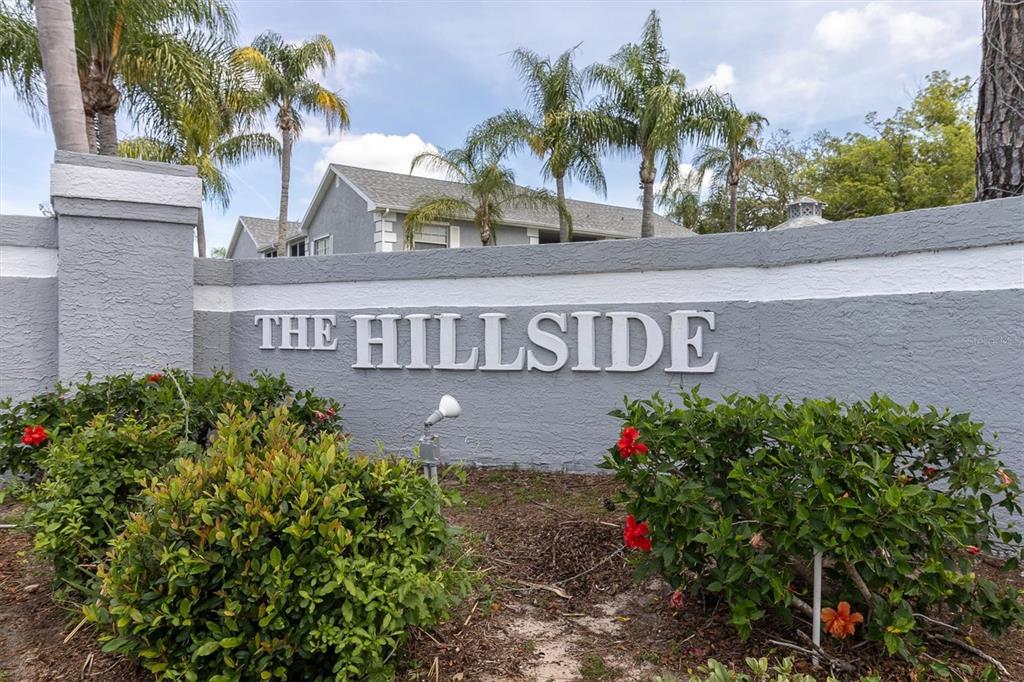 A gray stucco wall displays the sign The Hillside in front of palm trees — 7712 HILLSIDE COURT UNIT 201, HUDSON, FL