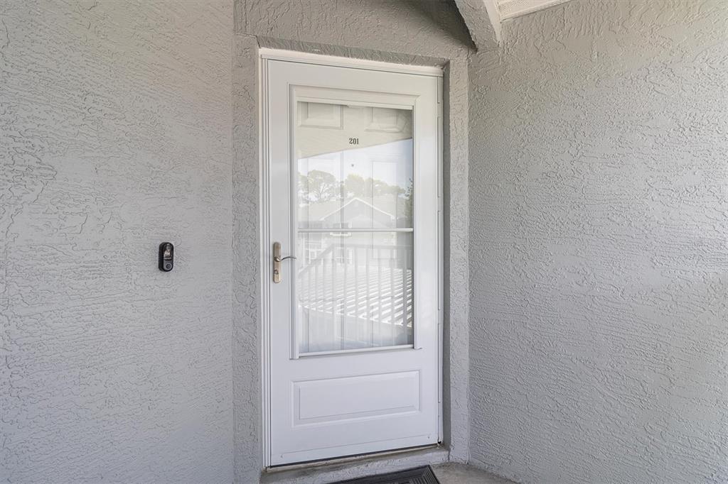 A white storm door with the number 201 is set into a gray stucco exterior wall — 7712 HILLSIDE COURT UNIT 201, HUDSON, FL