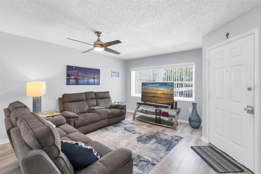 A living room features gray sofas, a television on a stand, and a ceiling fan — 7712 HILLSIDE COURT UNIT 201, HUDSON, FL
