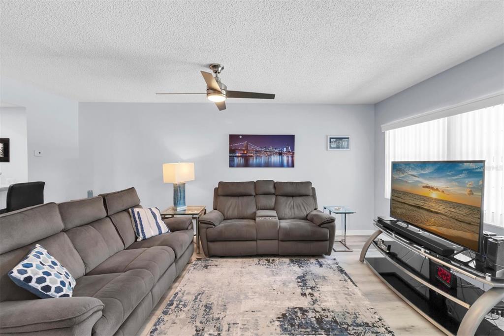 A living room featuring grey sofas, a patterned area rug, and a television on a stand — 7712 HILLSIDE COURT UNIT 201, HUDSON, FL