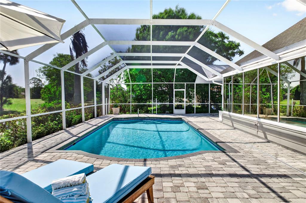 A screened-in swimming pool with a paver deck and lounge chairs under a white enclosure — 770 PELICAN BAY DRIVE, DAYTONA BEACH, FL
