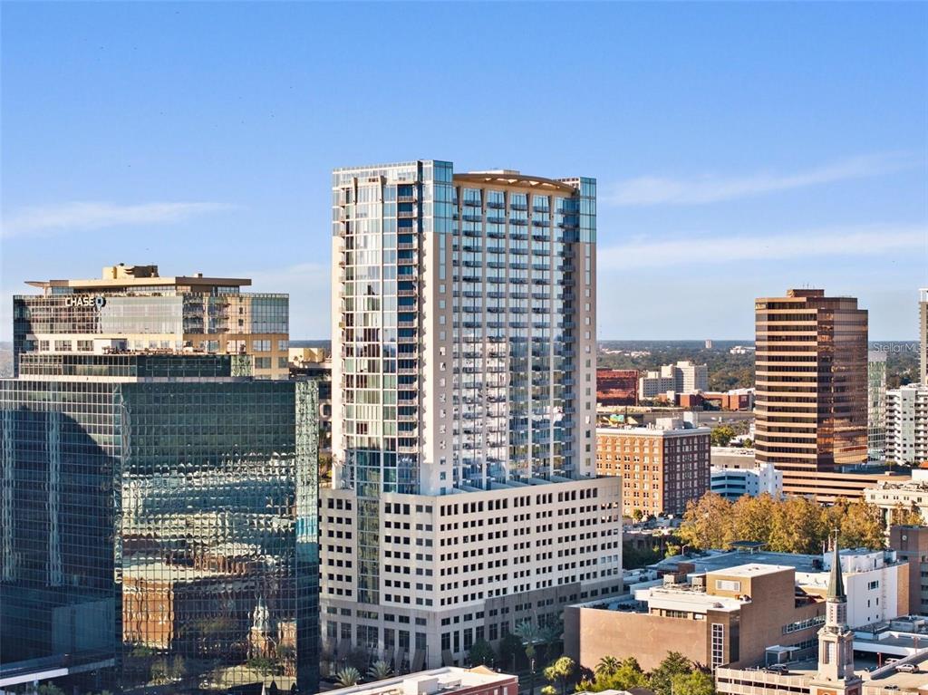 An exterior view of a tall residential high-rise building surrounded by other city skyscrapers — 155 S COURT AVENUE UNIT 1705, ORLANDO, FL