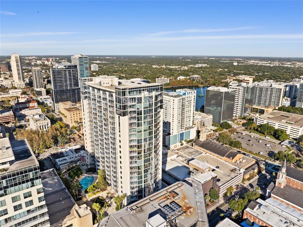 An aerial view shows a tall, modern residential tower surrounded by other city buildings — 155 S COURT AVENUE UNIT 1705, ORLANDO, FL