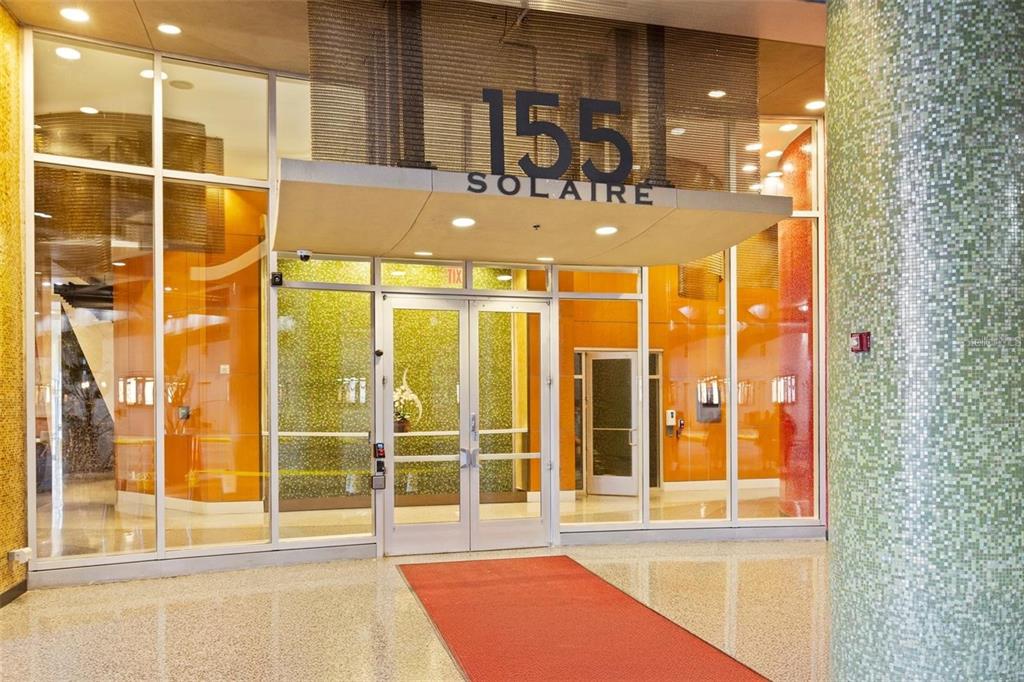 The entrance to a modern building features glass doors, orange walls, and a tiled column — 155 S COURT AVENUE UNIT 1705, ORLANDO, FL