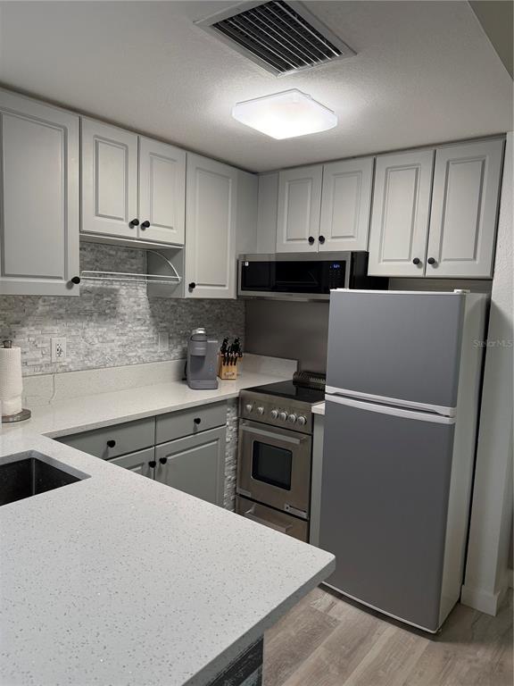 A kitchen features gray cabinets, stainless steel appliances, and light-colored countertops — 6165 CARRIER DRIVE UNIT 3106, ORLANDO, FL