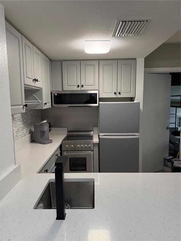 A kitchen features light gray cabinets, stainless steel appliances, and white quartz countertops — 6165 CARRIER DRIVE UNIT 3106, ORLANDO, FL