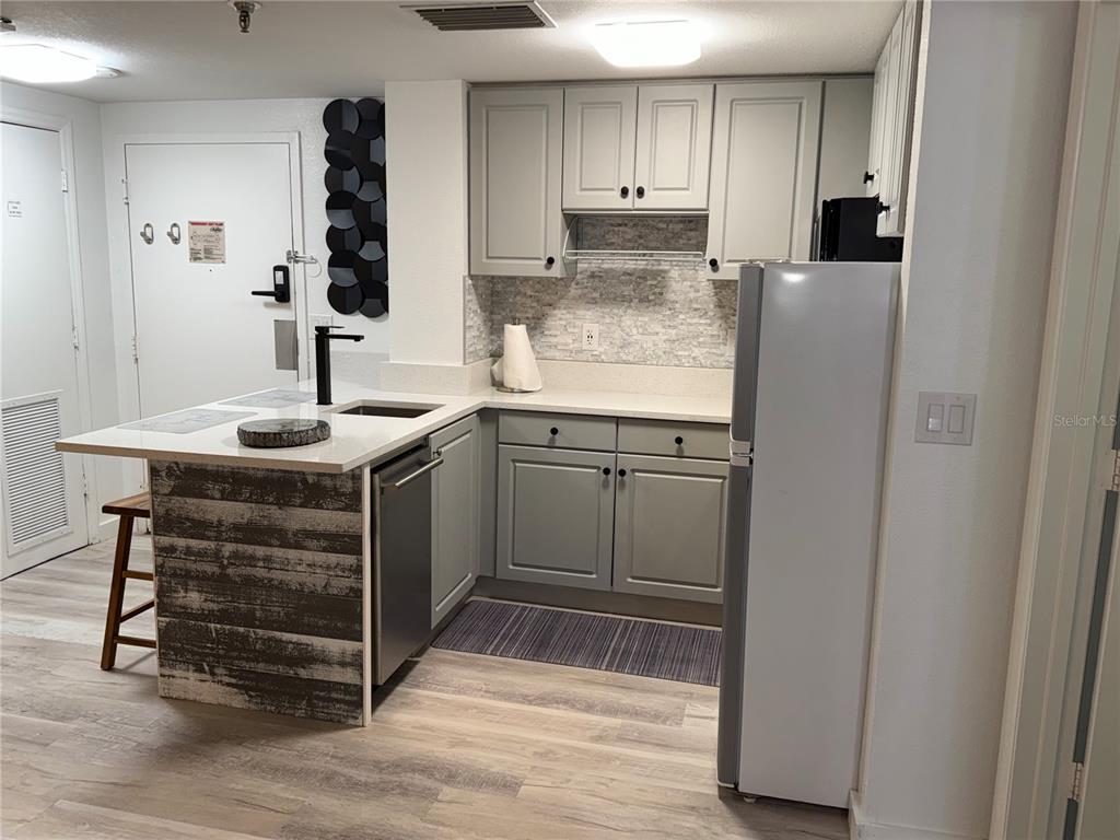 A kitchen features gray cabinets, stainless steel appliances, a white countertop, and a wood-paneled island — 6165 CARRIER DRIVE UNIT 3106, ORLANDO, FL